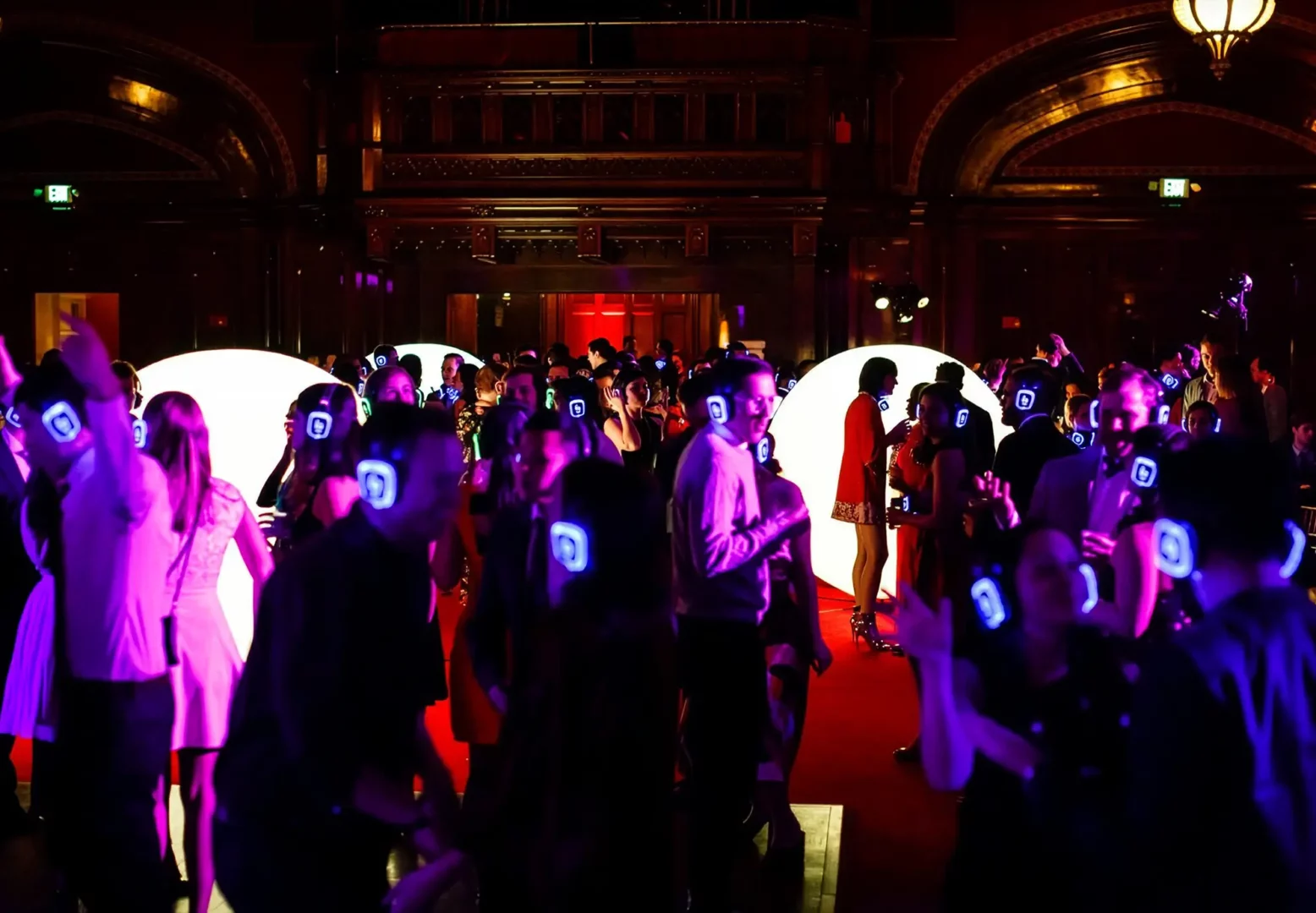 Guests in glowing headphones dancing under colorful lights.