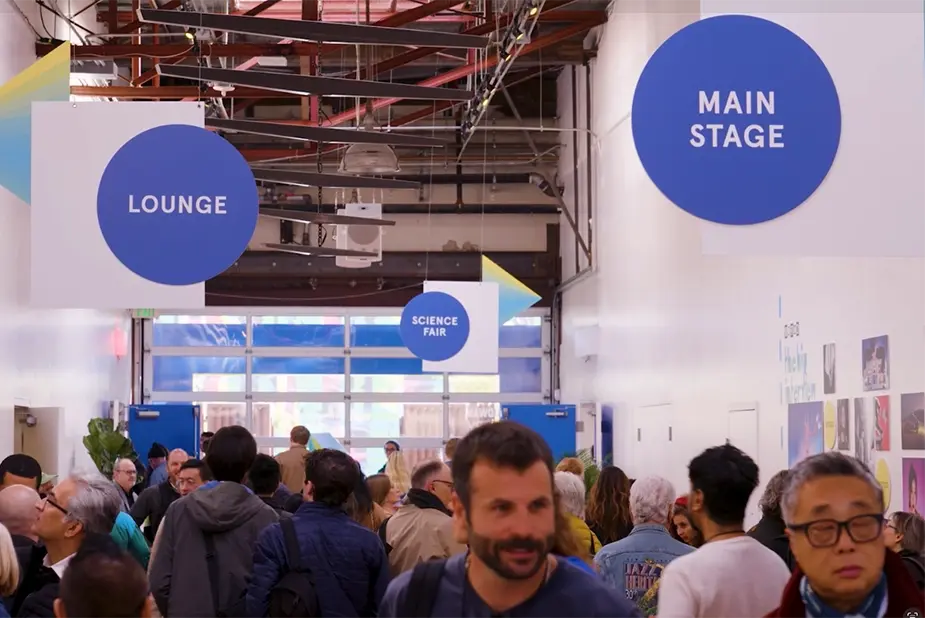 Crowded event hallway with lounge and main stage signs